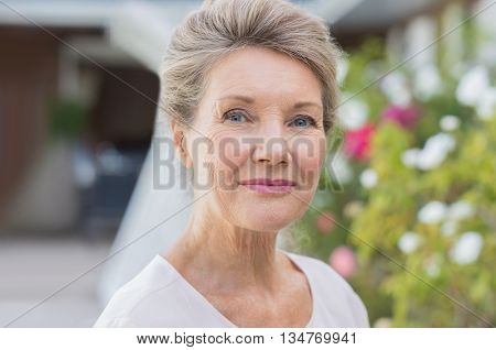 Portrait of a happy old senior woman looking at camera. Outdoor portrait of smiling retired woman. Close up face of a smiling elderly woman ouside the house.