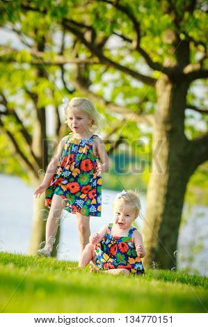 sisters playing outside in park by lake wearing matching outfits beautiful dresses
