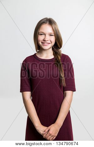 Portrait of cute cheerful young woman in vinous dress on light grey background