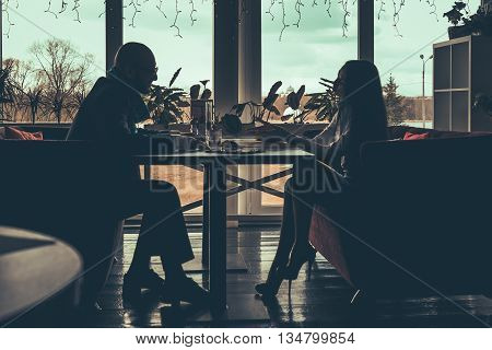 The silhouette of the love couple sitting at table in a cafe