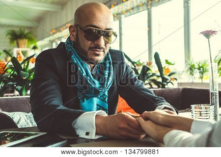 Arab man and the stylish girl sitting and holding hands in the restaurant