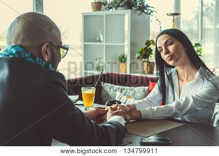 Arab man and the stylish girl sitting and holding hands in the restaurant