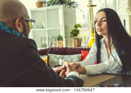 Arab man and the stylish girl sitting and holding hands in the restaurant
