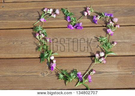 Heart in flowers on wooden floor in summer