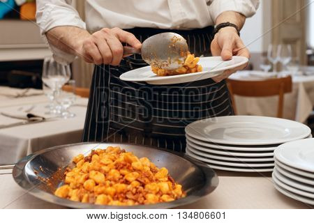 Chef is putting gnocci with meat in plates, serving restaurant guests