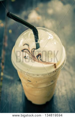 Iced blended frappucino in plastic cup on wood background. Iced coffee. Vintage color tone.