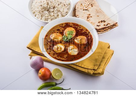 egg curry with roti/chapati and jeera rice, tasty and spicy anda curry with roti and rice, indian egg masala curry served in ceramic bowl with roti, salad and jeera rice