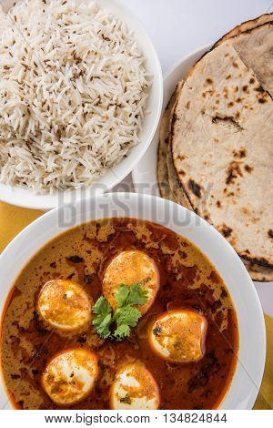 egg curry with roti/chapati and jeera rice, tasty and spicy anda curry with roti and rice, indian egg masala curry served in ceramic bowl with roti, salad and jeera rice