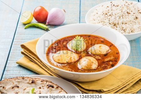 egg curry with roti/chapati and jeera rice, tasty and spicy anda curry with roti and rice, indian egg masala curry served in ceramic bowl with roti, salad and jeera rice