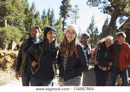 Group of six friends hiking past a log cabin in a forest
