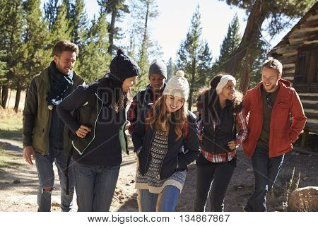 Group of friends talk as they hike past a cabin in a forest