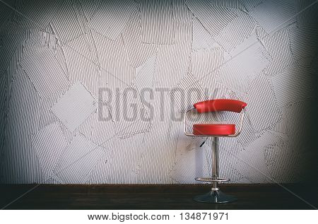 modern red chair in an empty room. in the circle of light there is red swivel chair on a background of gray wall with decorative relief plaster. copy space for your text