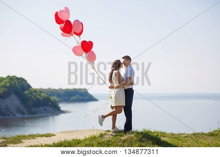 Romantic wedding couple standing on a cliff with red air-balloons