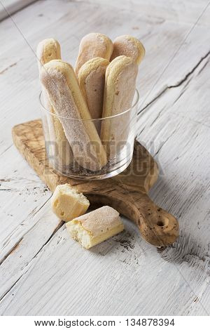 Sweet pastries, biscuits Savoiardi, ladies fingers in a glass mug on a light plain wooden background. selective focus