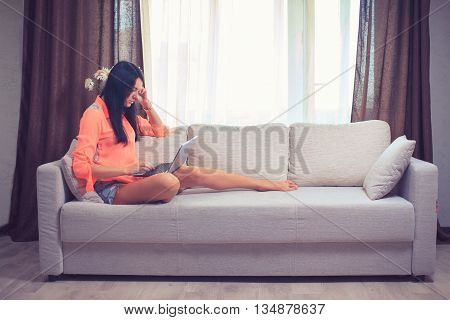 Happy young woman is relaxing on comfortable couch and using laptop at home. Photo toned