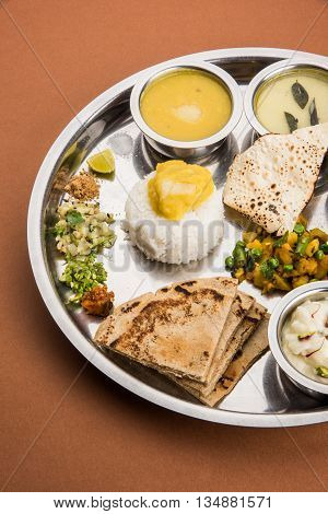 typical maharashtrian food served in a steal plate, marathi food includes kadhi and shrikhand, plain dal, spinach curry, aalu mutter, plain rice, papad, bhakri or bhakar or roti and variety of salad