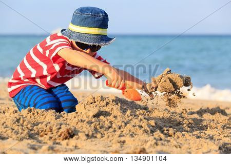 happy cute little boy play with sand on beach
