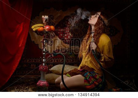 Young woman dressed in hippie style smoking hookah