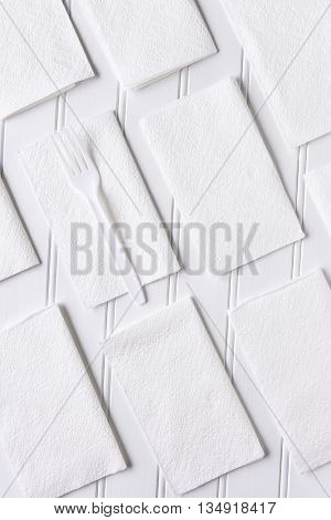 White Napkins on a White Table. A single plastic fork on one napkin. Vertical format from a high angle.