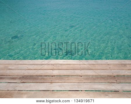 Unique perspective wooden slat floor with green crystal sea water surface ripple and sun reflection. Water background. Ocean water texture.
