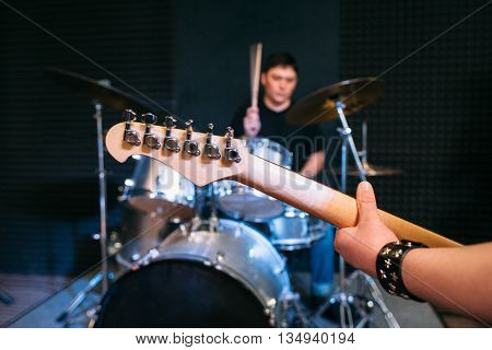 Guitar neck close-up on drum set background . Focus on guitar neck and guitar player hand, drummer playing on drums on background. Alive performance