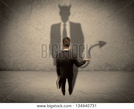 An experienced tricky businessman in suit looking at his devil desguise shadow reflected on the wall concept