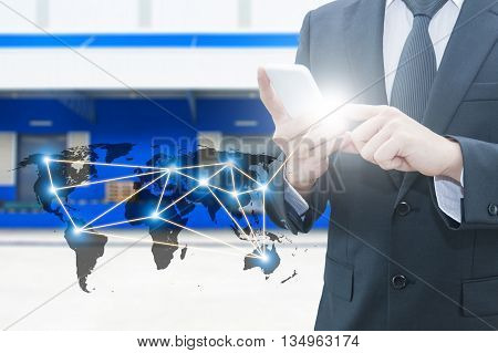 Double exposure of businessman using smart phone network connection world map , transportation port and blurred cargo warehouse background international transportation trading business concept