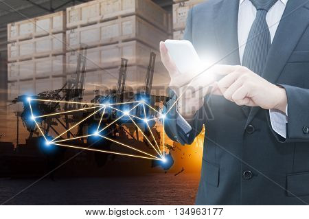 Double exposure of businessman using smart phone network connection world map , transportation port and blurred cargo warehouse background international transportation trading business concept