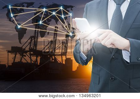 Double exposure of businessman using smart phone network connection world map , transportation port and blurred cargo warehouse background international transportation trading business concept