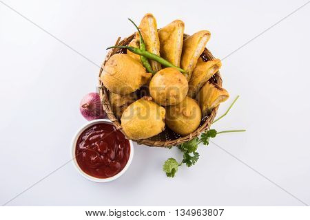 batata vada or aalu bonda or aalu bonde and bread pakoda or bread pakode served in a cane basket with tomato ketchup, onion and coriander over white background, isolated