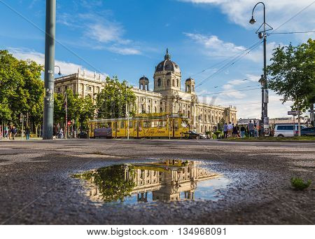 VIENNA AUSTRIA - 12TH JUNE 2016: The outside of the KH Museum in Vienna and a Yellow Ring Tram. Reflections can be seen in a puddle. People can be sen in the distance.