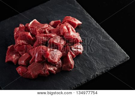 Pieces of raw fresh meat isolated on black stone board on side of the image