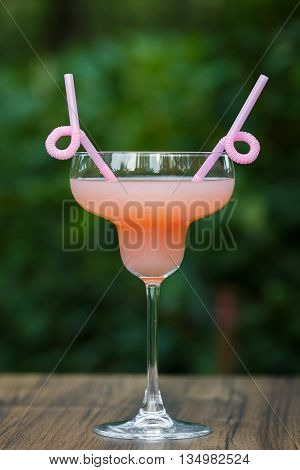 Glass of cold pink cocktail with straw on green background bokeh