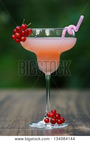 Glass of cold pink cocktail with straw on green background bokeh