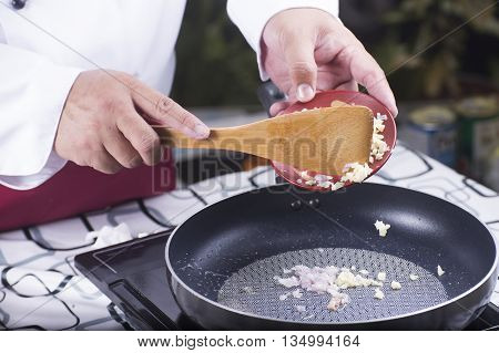 Chef putting garlic and red onuion to the pan / cooking spaghetti concept