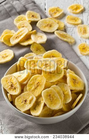 Heap Of Dried Banana Chips Snack In White Bowl On Rustic Table With Grey Napkin