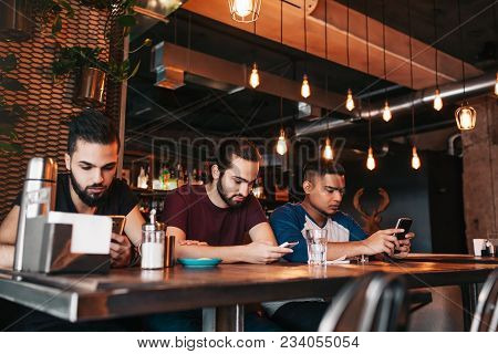 Social Media Addiction Concept. Mixed Race Friends Looking At Their Phones In Lounge Bar. Loneliness