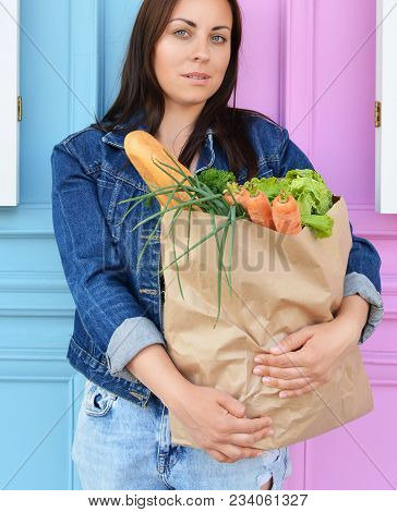 Girl In A Jeans Jacket Is Holding A Paper Bag With Food In Her Hands. The Woman Stinted In The Super