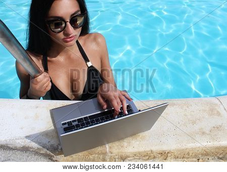 Sexy Girl In A Black Bikini Uses A Laptop With A Black Screen In The Pool. Work On Vacation. Glamoro