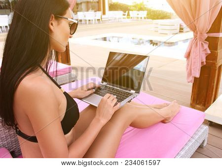 Incredibly Sexy Girl In A Black Bikini Sits With A Laptop Near The Pool.