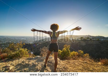 athletic african american woman celebrating reaching top of runyon canyon with arms open