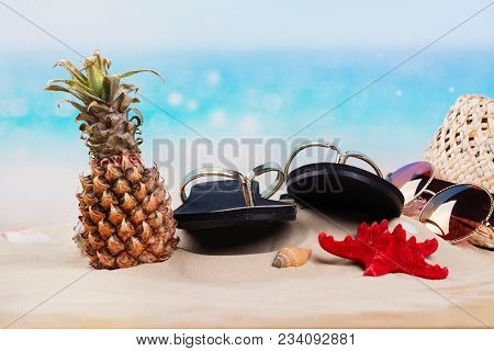 Flip Flops, Hat, Mini Pineapple And Sunglesses On Sandy Beach. Travel, Vacation, Holidays Background