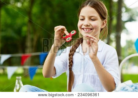 Happy and carefree girl in white cotton blouse playing with fidget spinner in park on summer day