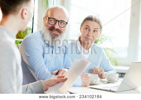 Senior colleagues looking at young businessman with papers while discussing financial situation at meting in cafe