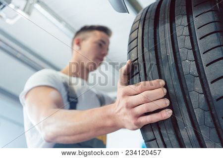 Low-angle view of the hand of a skilled auto mechanic holding a new high-quality tire during work in a modern automobile repair shop