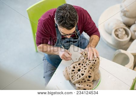 Topview of Ceramist Dressed in an Apron Sculpting Statue from Raw Clay in the Bright Ceramic Workshop.