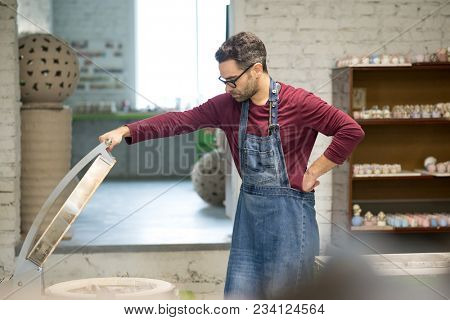 Ceramist Dressed in an Apron Setting the Electric Oven for Drying the Clay Sculpture Using the Control Console.