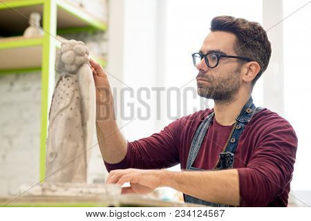 Portrait of Ceramist Dressed in an Apron Working on Clay Sculpture in the Bright Ceramic Workshop.