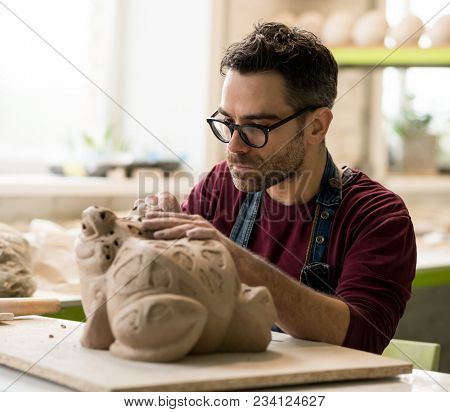 Ceramist Dressed in an Apron Sculpting Statue from Raw Clay in the Bright Ceramic Workshop.