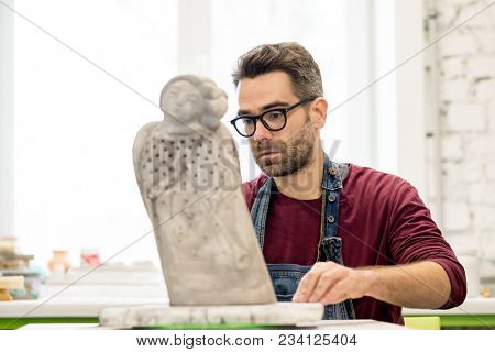 Portrait of Ceramist Dressed in an Apron Working on Clay Sculpture in the Bright Ceramic Workshop.